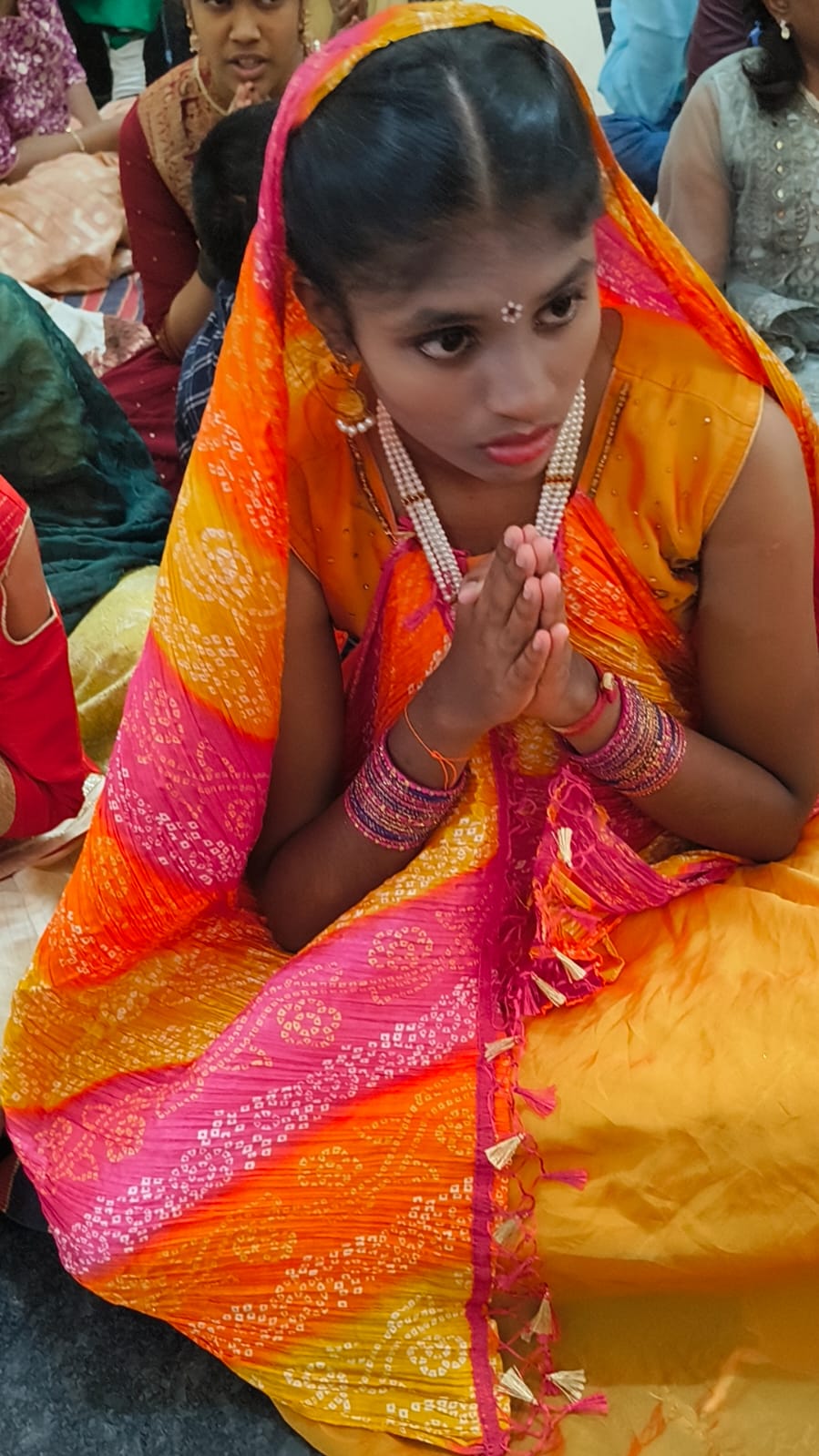 A student in festive attire with hands folded in prayer during the Janmashtami celebration